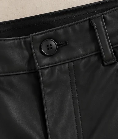 Detalhe do botão preto de quatro furos e do fechamento do Shorts Couro Eco, com costuras aparentes